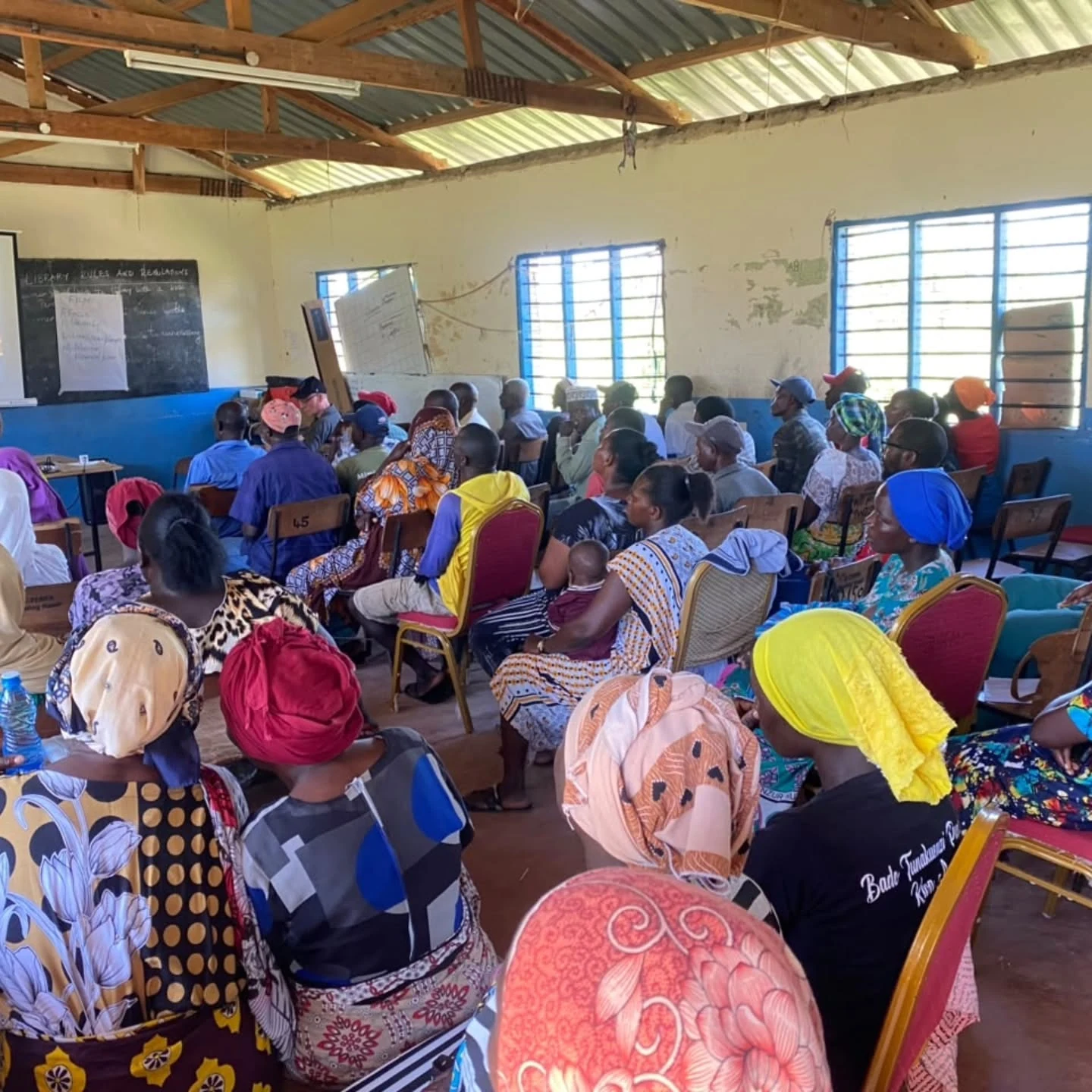 Adults and young people sit together in a village classroom during an Amka Nawi gathering.
