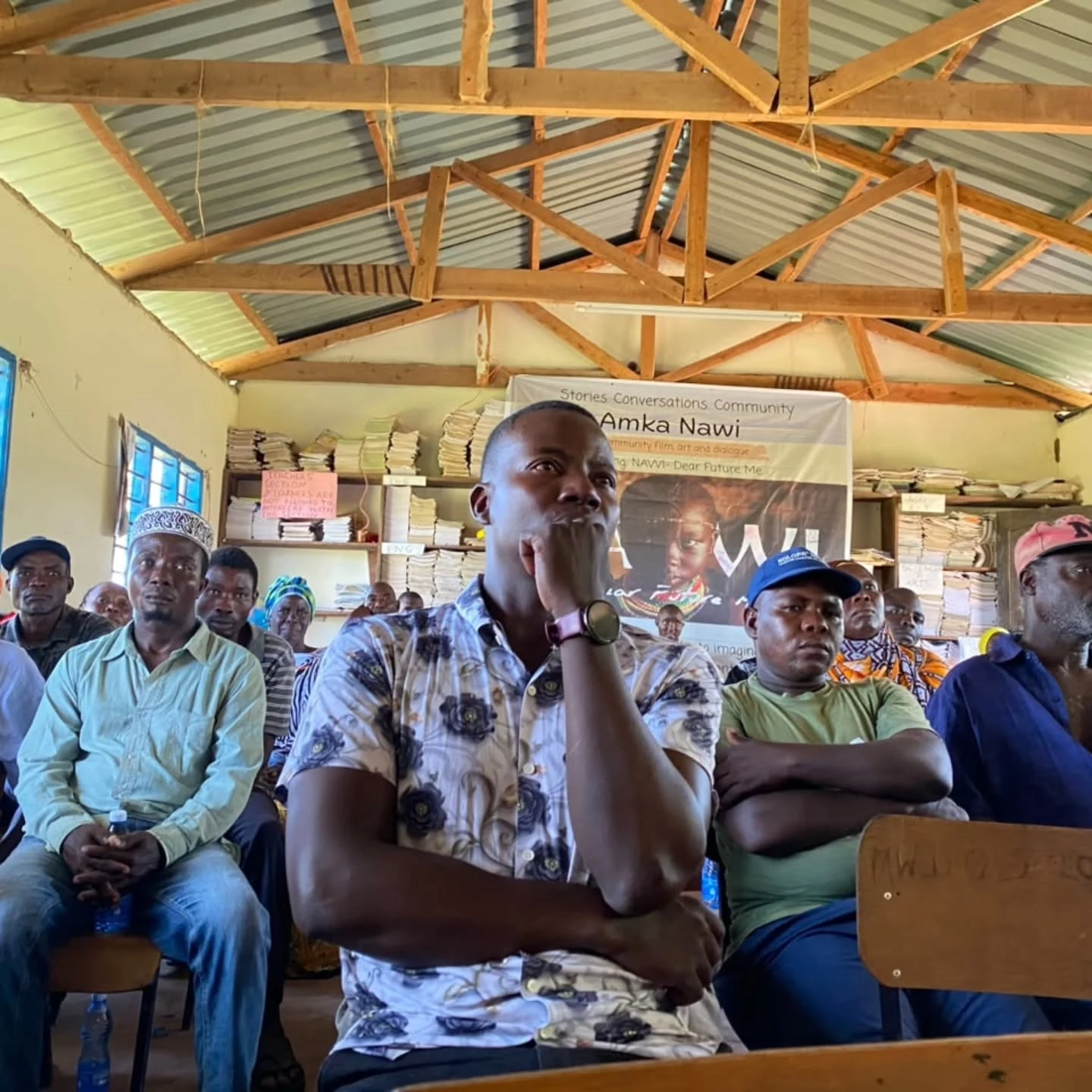 Community members listen together during an Amka Nawi conversation beneath the project banner.