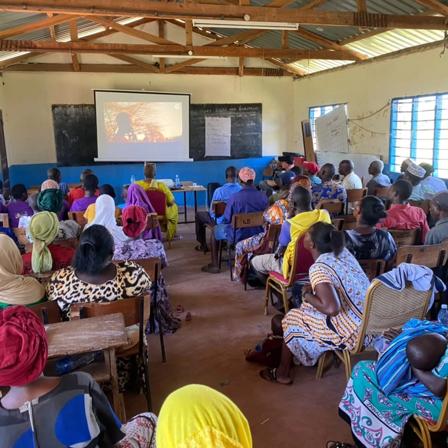 A village audience faces a projected NAWI film during a community screening.